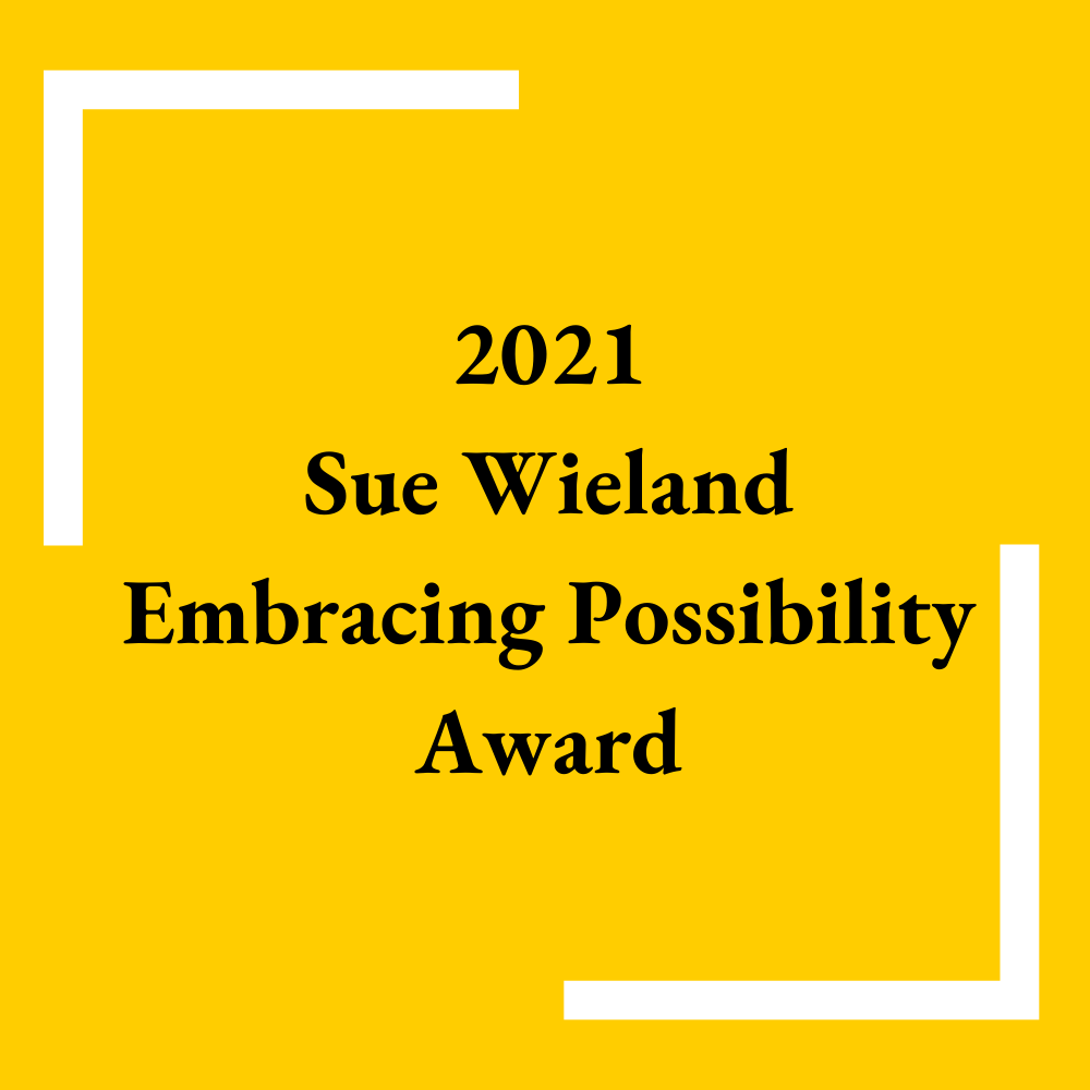 A dark yellow square with white L shape brackets in the top left hand corner and bottom right hand corner. In between the brackets in black letters is written 2021 Sue Wieland Embracing Possibility Award.