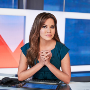HLN's Robin Meade headshot. Robin sitting at a news desk in a teal short sleeve top with her hands clasped in front of her.