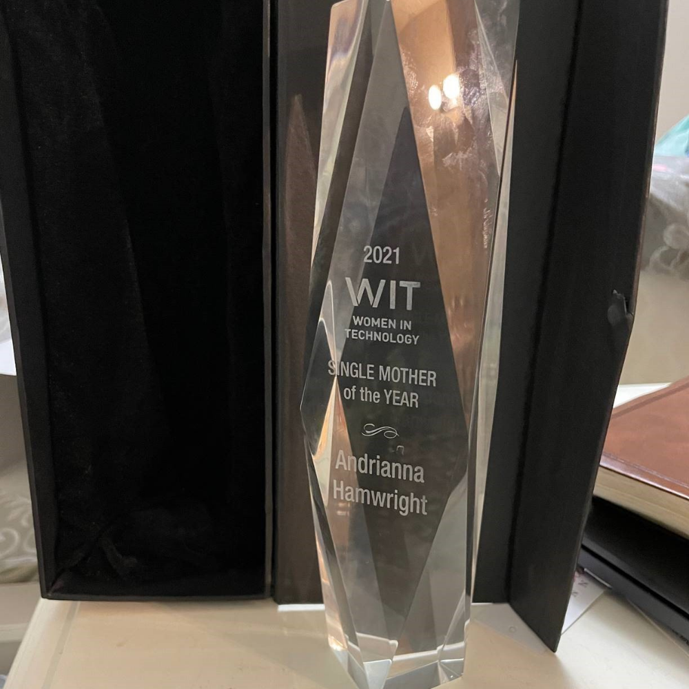 Tall glass award on a desk with the words: 2021 WIT Women in Technology SINGLE MOTHER of the YEAR Andrianna Hamwright 